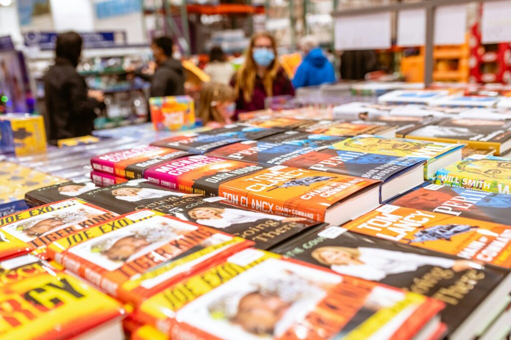 a table full of children's books with people in the background inside a Costco