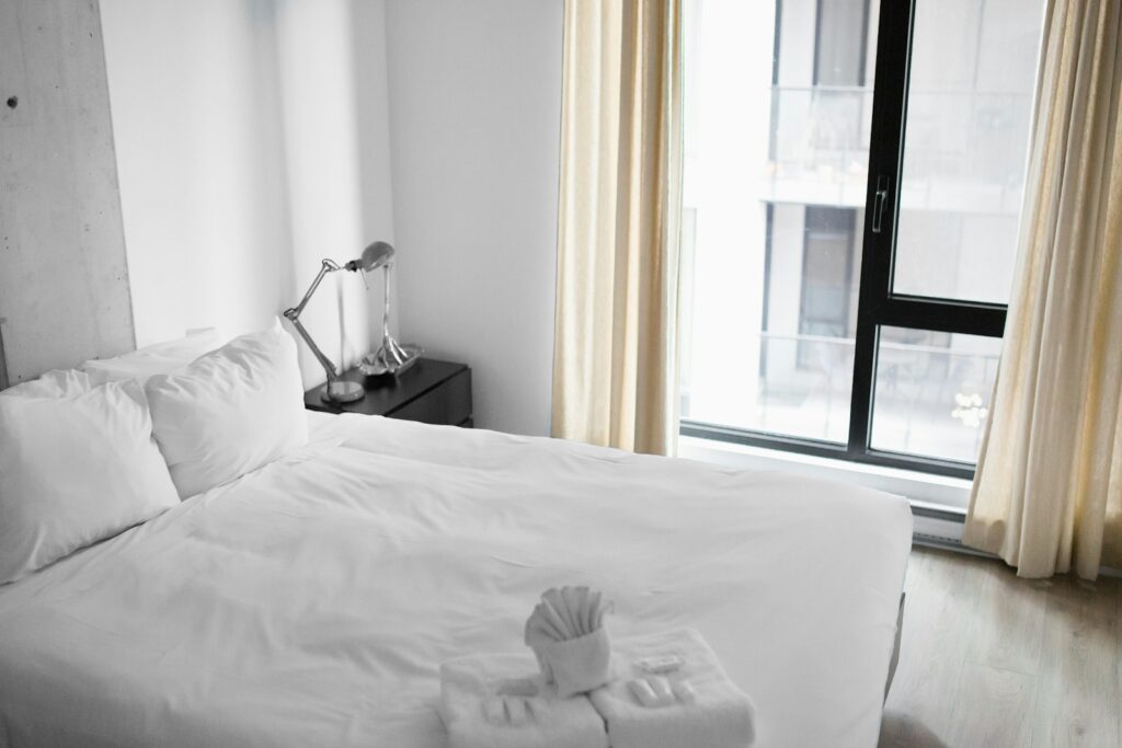 a vacant white bed near an open window in a clean hotel room