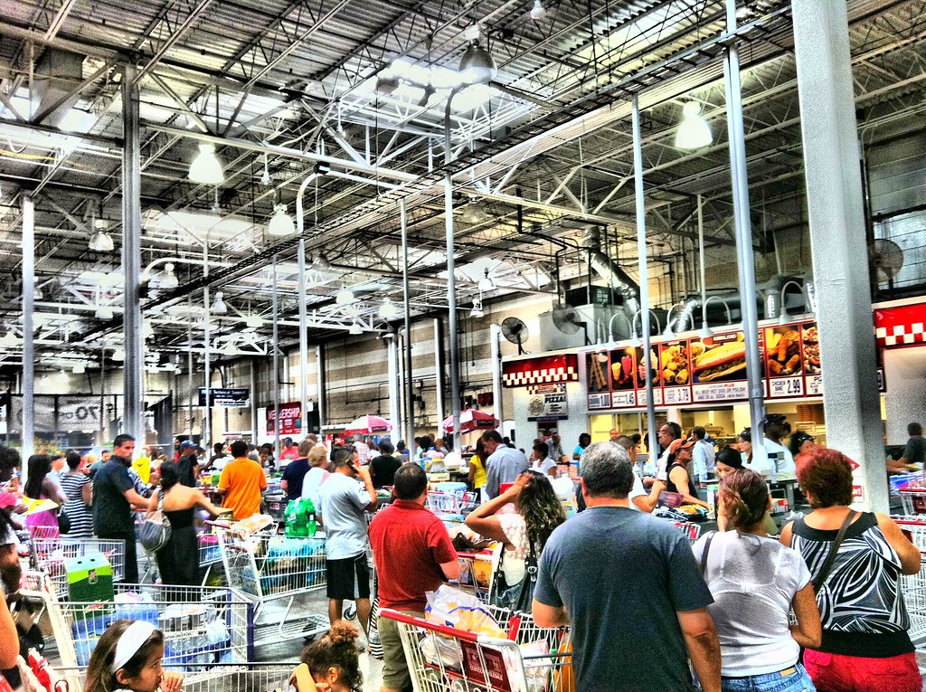 A crowd of people stand inside of a Costco store.