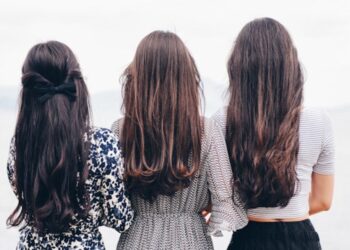 three woman looking back and facing body of water