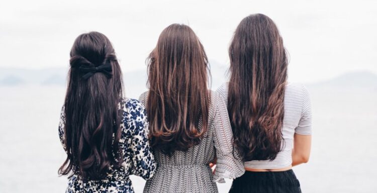 three woman looking back and facing body of water