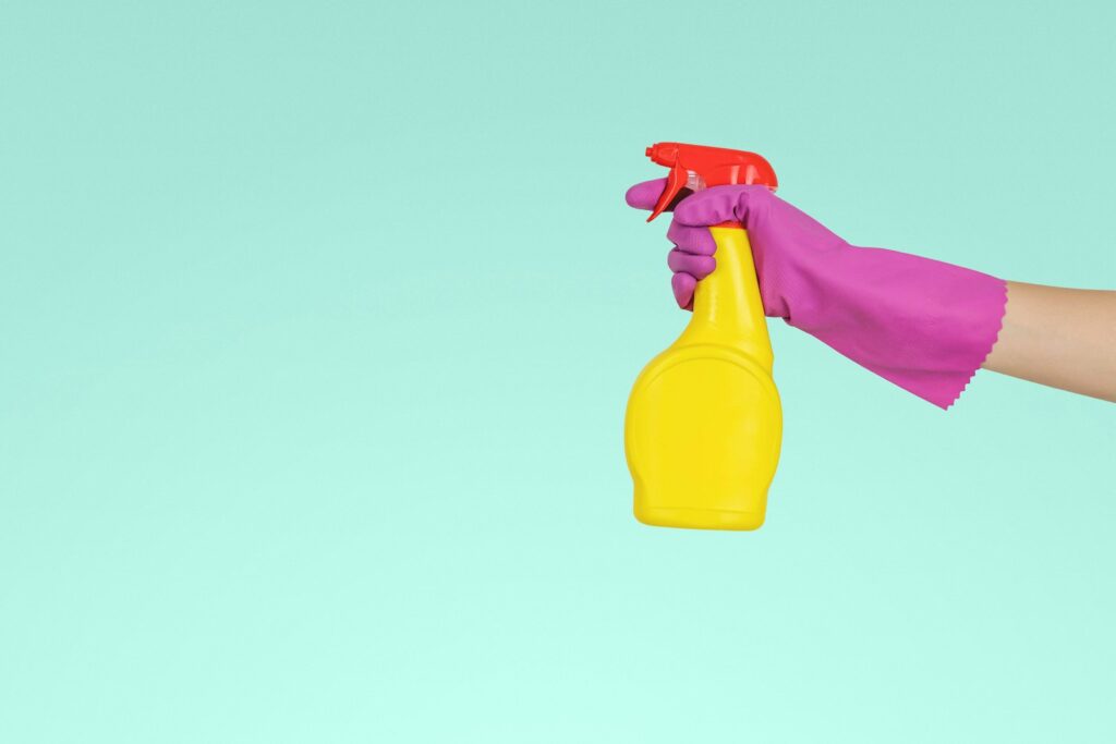 person holding yellow plastic spray bottle in front of a light blue background