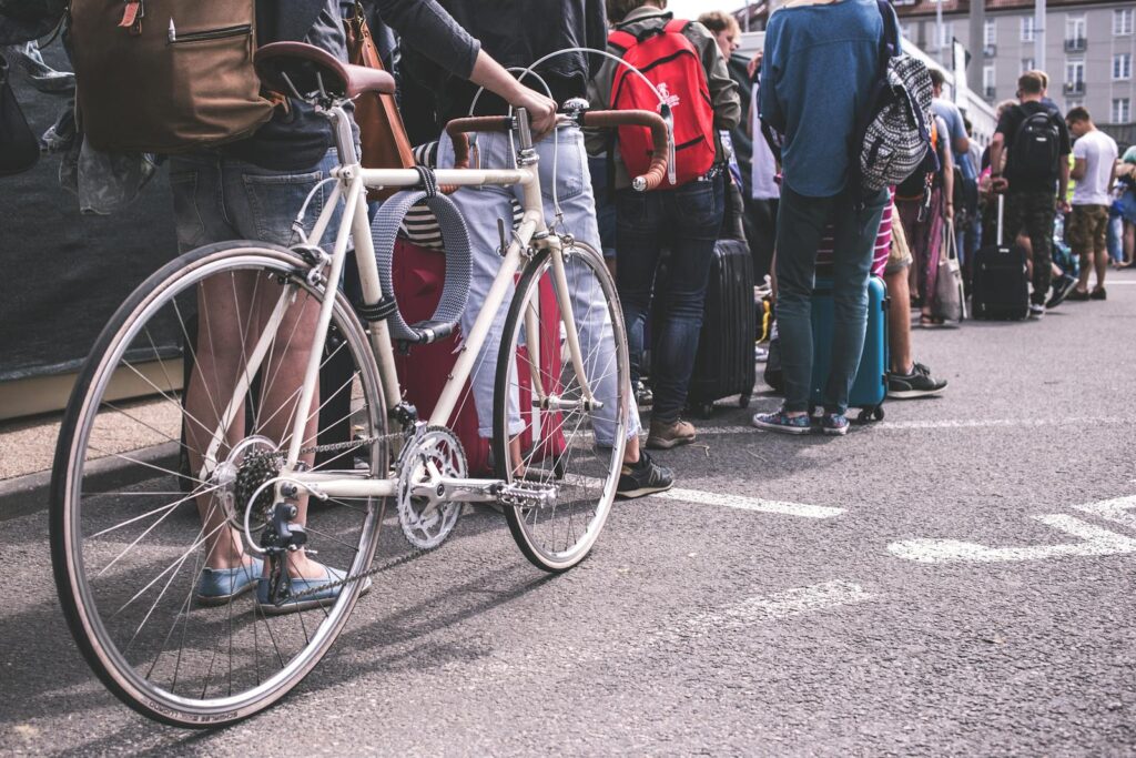 Person in Black Sweater Hold a Grey Road Bike while waiting in a line of people