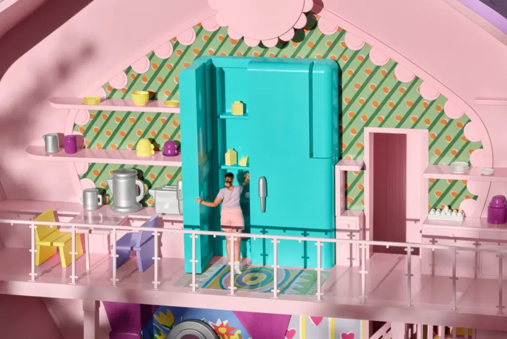 A woman opens the door to an oversized dollhouse version of a fridge