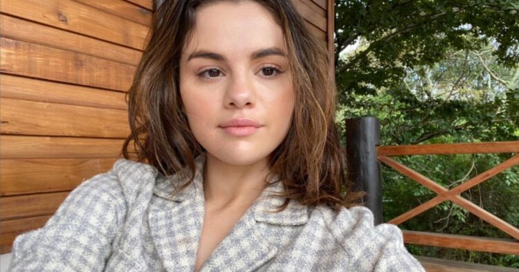 Selena Gomez taking a selfie, while sitting on a deck at a cottage.