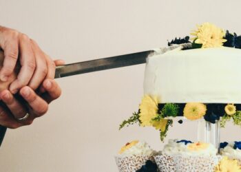 couple both holding knife slicing a cake on tray