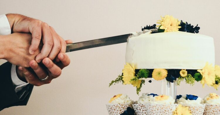 couple both holding knife slicing a cake on tray
