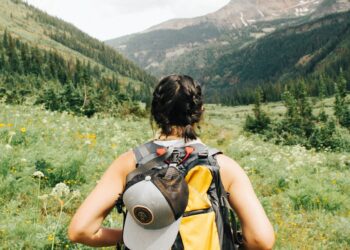 person carrying yellow and black backpack walking between green plants