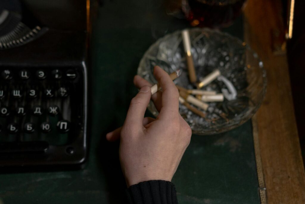 Hand Holding a Cigarette and a Vintage Typewriter