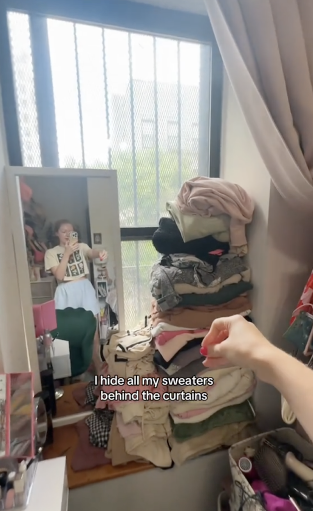 A woman holding a camera up to a stack of folded clothing in a bedroom.