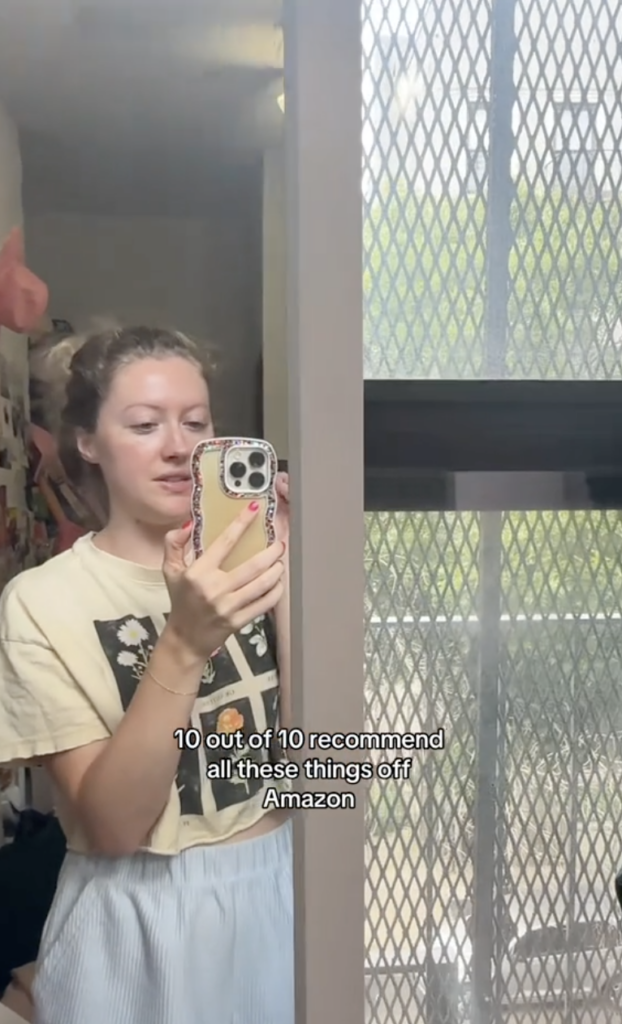 A woman standing in a bedrom with her phone in hand.