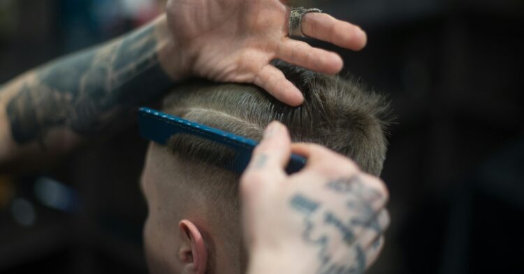 man with tattoos cutting another man's hair