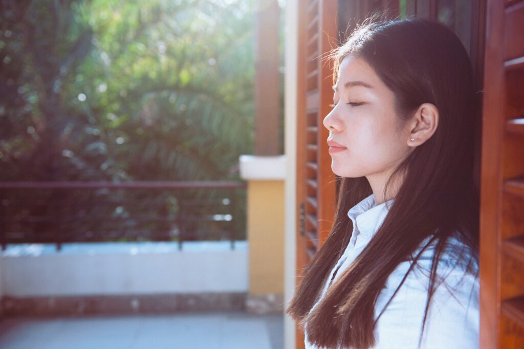 a woman standing next to a window with her eyes closed
