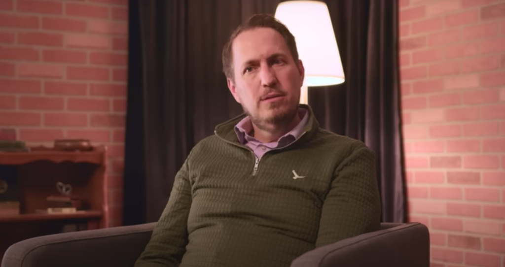 A man in a green sweater is interviewed 