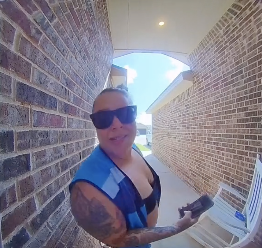 woman standing in front of the front door of a house holding a phone while looking into a doorbell camera