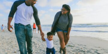man in black and white striped long sleeve shirt holding baby in white shirt on beach