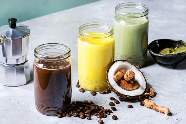Variety of iced colorful latte drinks Iced coffee, turmeric and matcha latte cocktails in glass jars with ingredients above over grey green texture background Copy space