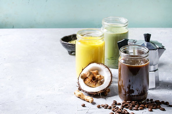Variety of iced colorful latte drinks Iced coffee, turmeric and matcha latte cocktails in glass jars with ingredients above over grey green texture background Copy space