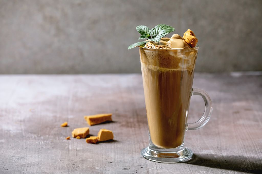 Dalgona frothy coffee trend korean drink latte espresso with coffee foam in tall glass. decorated by dalgona cinder toffee candy and mint. Grey concrete background.