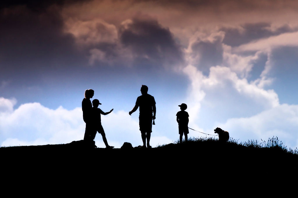 A family and their pet dog seen in silhouette walking in the late evening sunlight on Pentire Point East in Newquay in Cornwall