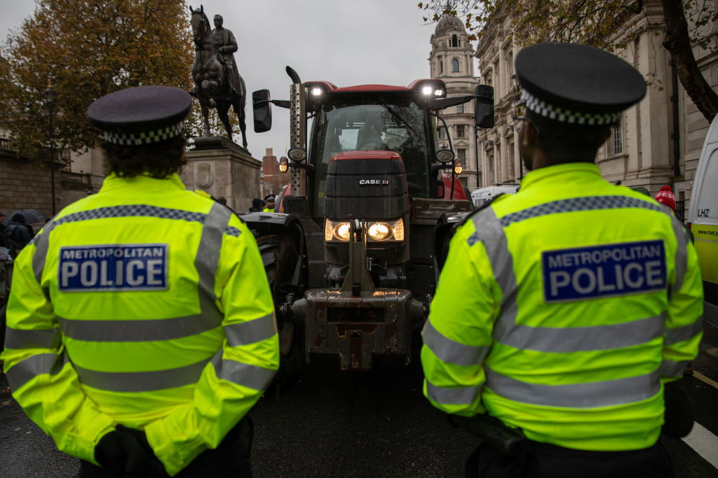 Metropolitan Police officers stand in-front of a red tractor...
