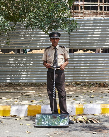 Security guard with mirror to detect bombs underneath cars