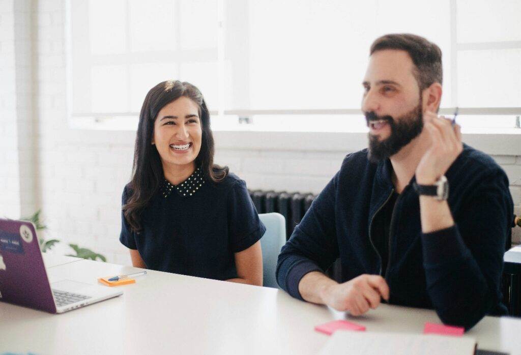 Two people smiling in work office (Unsplash | Jason Goodman)