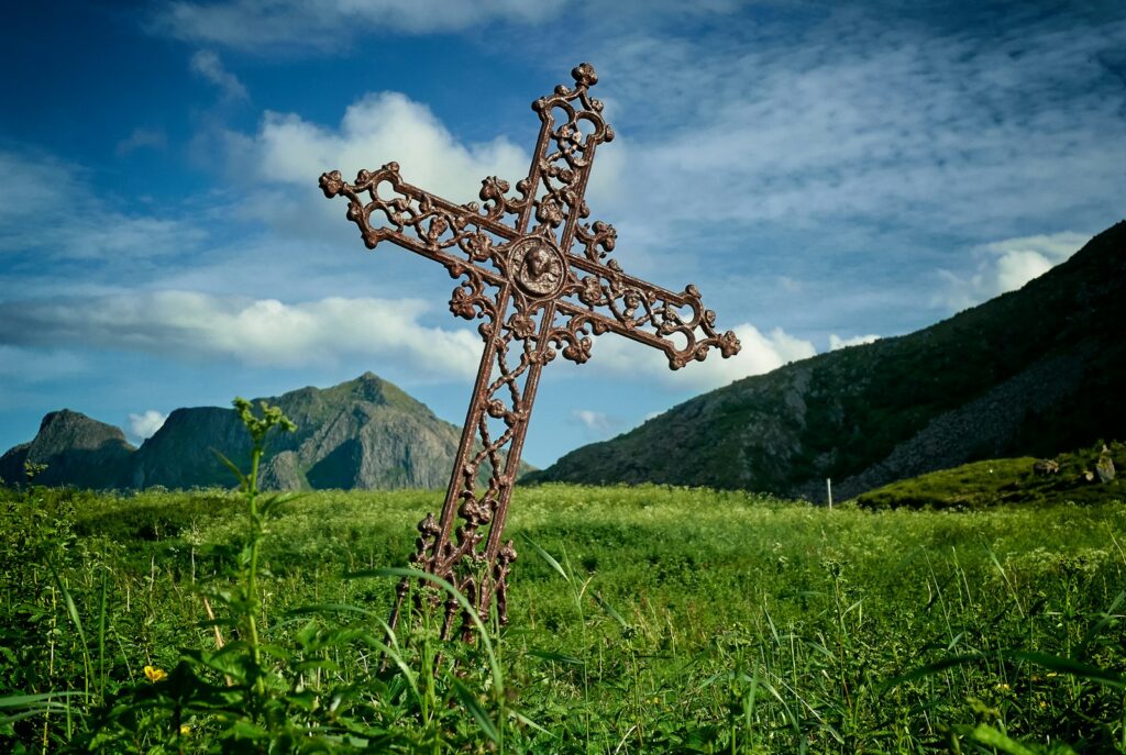 leaning brown metal cross on green grass field near mountains at daytime