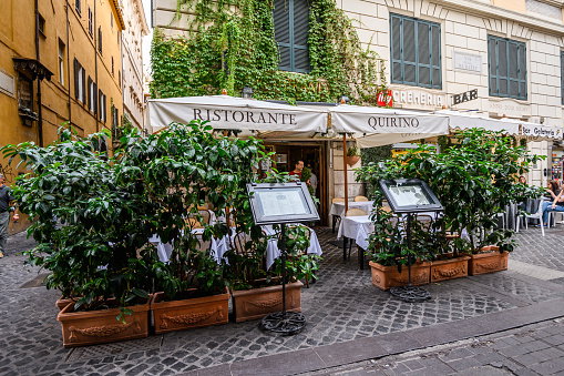 Atmospheric street cafe on a street in the center of Rome. Pots with trees. 28.10.2019 Rome, Italy