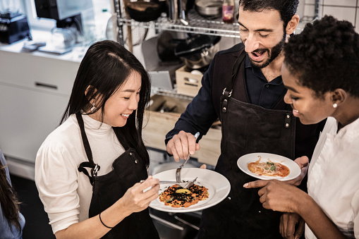 Smiling female chef standing with students holding food in cooking class