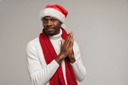 A young dark-skinned man in a woolen sweater, christmas hat and bright red scarf