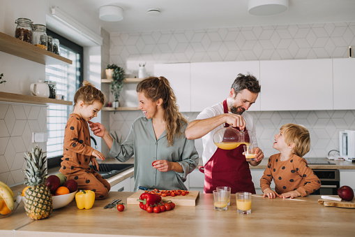 Young family with two little children preparing breakfast together in kitchen.