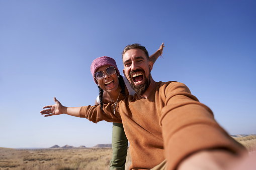 Enthusiastic photo of nomadic couple taking a selfie showing the desert to post it on social media apps.