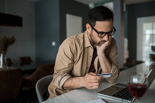 Worried man using his credit card to pay online and going broke.