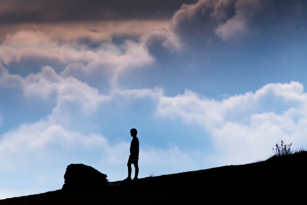 A young boy seen in silhouette standing alone in the late evening sunlight on Pentire Point East in Newquay in Cornwall