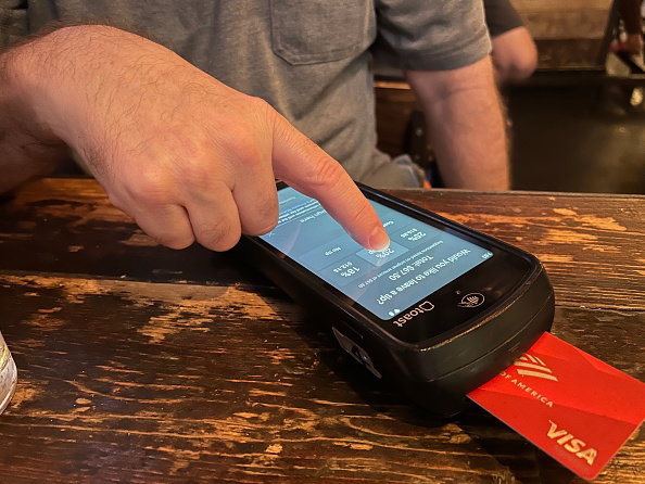 Man selecting 20% tip while using hand held credit card scanner at restaurant, Queens, New York