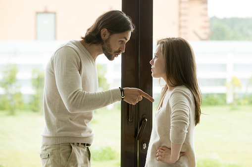 Young couple arguing at home, man pointing finger blaming woman