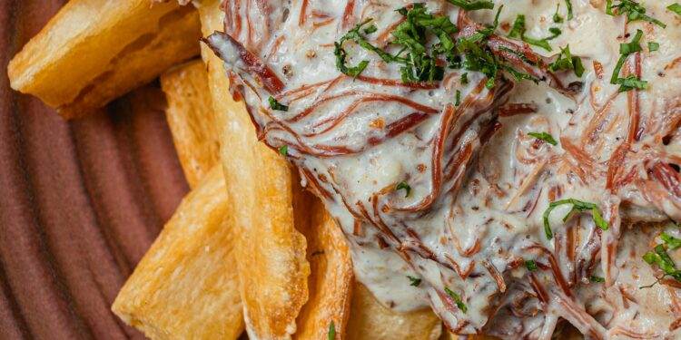 Close-up of Brazilian carne de sol with creamy sauce served on crispy cassava fries. A Maceió culinary delight.