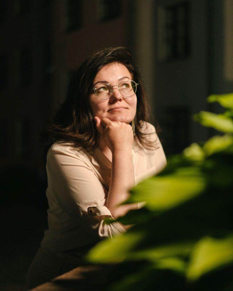 a woman with glasses sitting in front of a plant