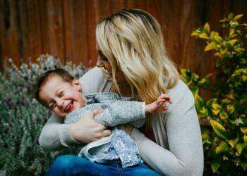 woman in gray sweater carrying girl in blue denim jacket