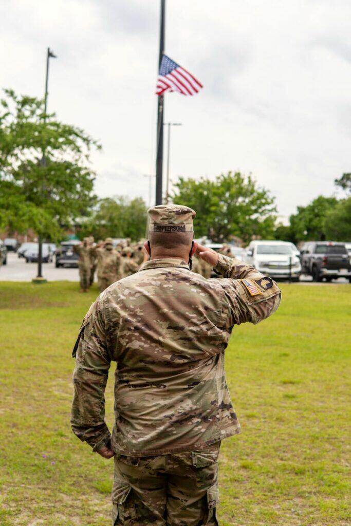 A soldier salutes the American flag at half mast during a ceremony outside.