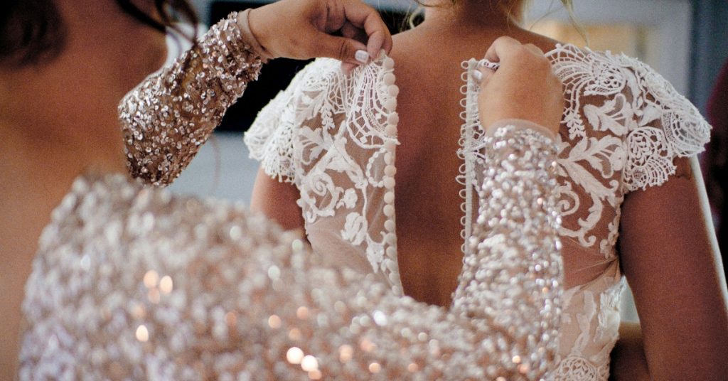 Someone zipping up bride dress