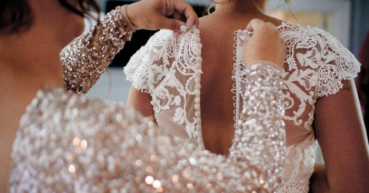 Someone zipping up bride dress