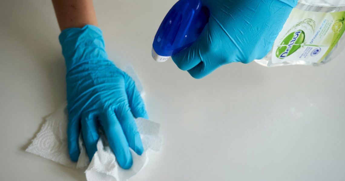 Person wearing blue gloves holding cleaning supplies