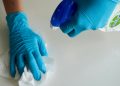 Person wearing blue gloves holding cleaning supplies