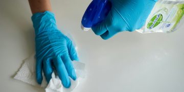 Person wearing blue gloves holding cleaning supplies