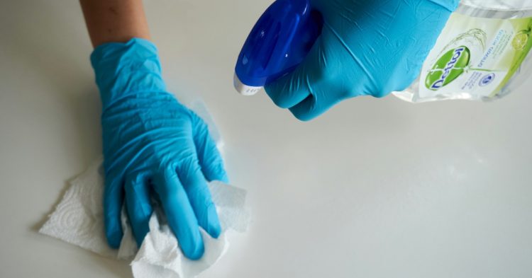 Person wearing blue gloves holding cleaning supplies
