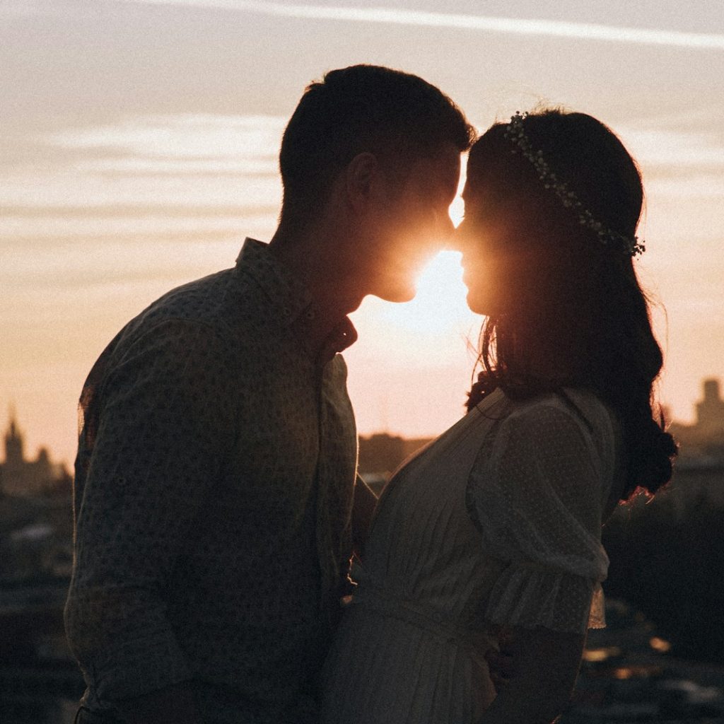 a man and a woman standing in front of a sunset