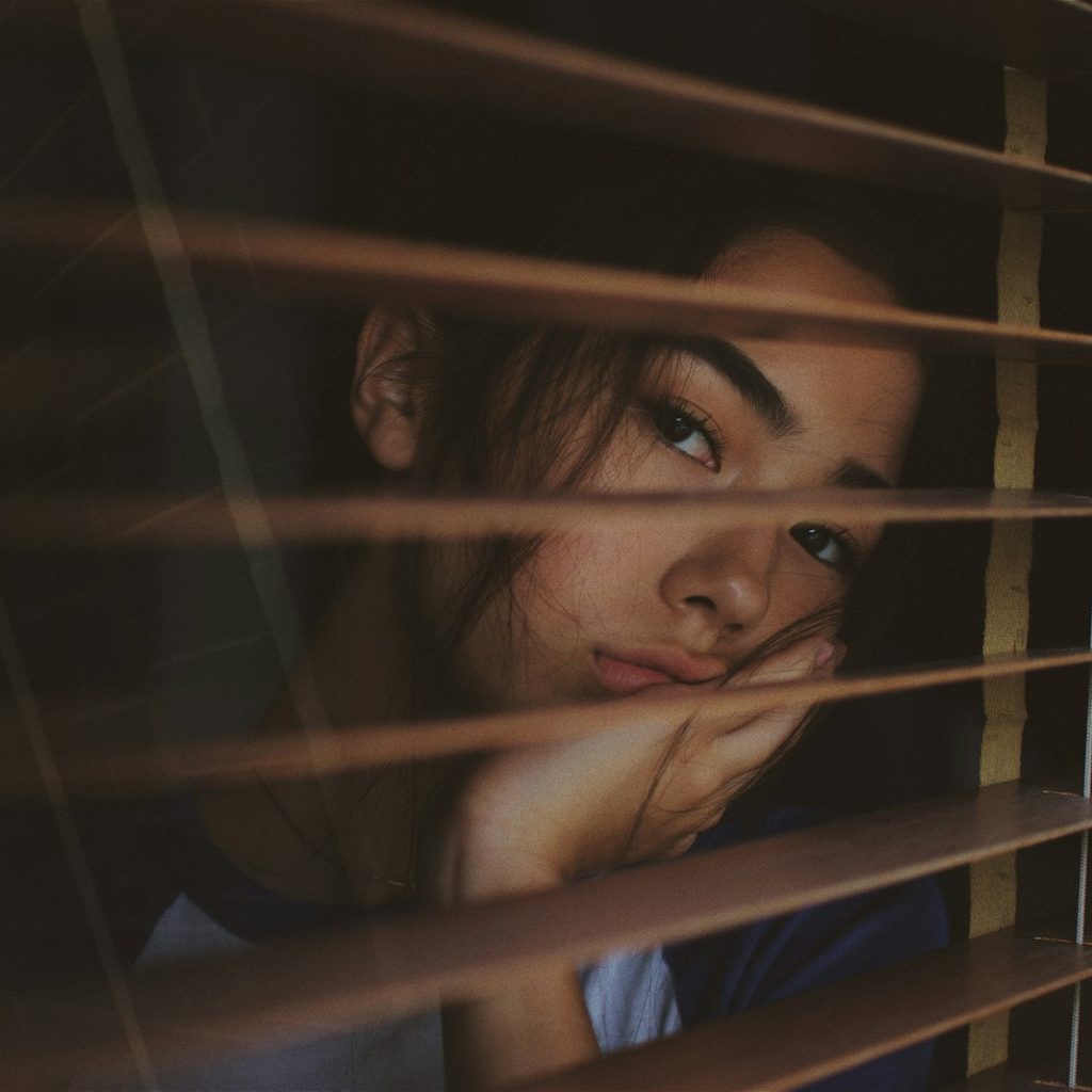 a woman looking out of a window with blinds